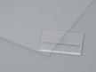 A clear acrylic film sample with 'CANAL PLASTICS CENTER' branding lying on a grey surface. 

Canal Plastics Center Clear acrylic film as a versatile material with numerous applications, offering a combination of weather resistance, moldability, and transparency in automotive, building, and display applications.
