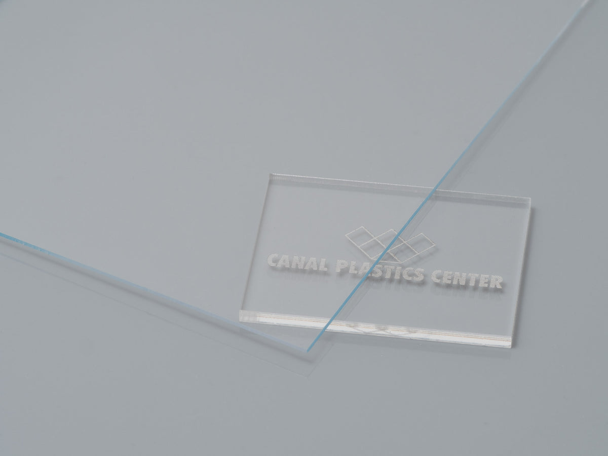 A clear acrylic film sample with 'CANAL PLASTICS CENTER' branding lying on a grey surface. 

Canal Plastics Center Clear acrylic film as a versatile material with numerous applications, offering a combination of weather resistance, moldability, and transparency in automotive, building, and display applications.