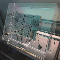 Electronic circuit board inside a clear acrylic box on a dark background. Canal Plastics